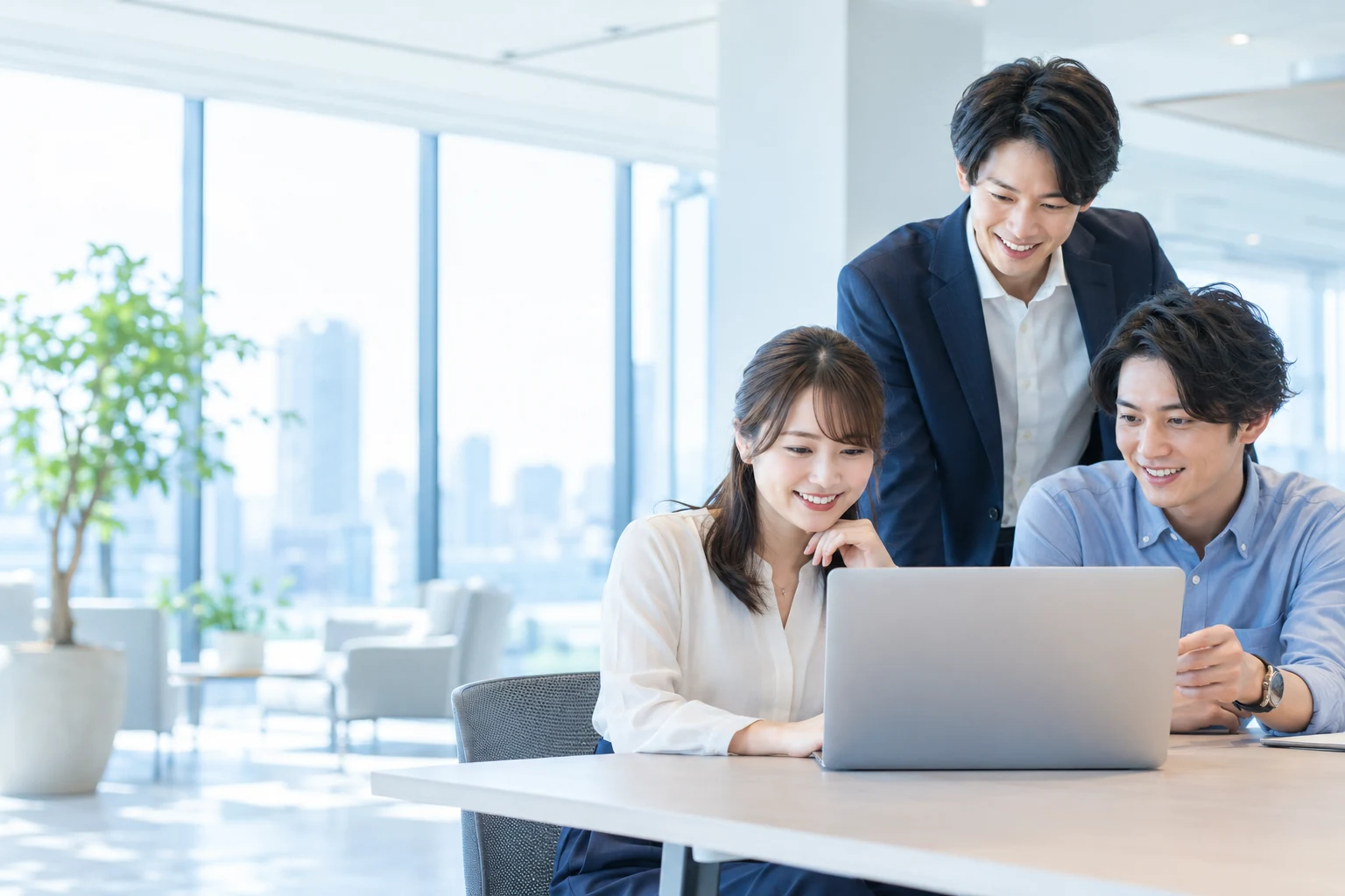 明るいオフィスでノートパソコンを囲み、打ち合わせをする3人